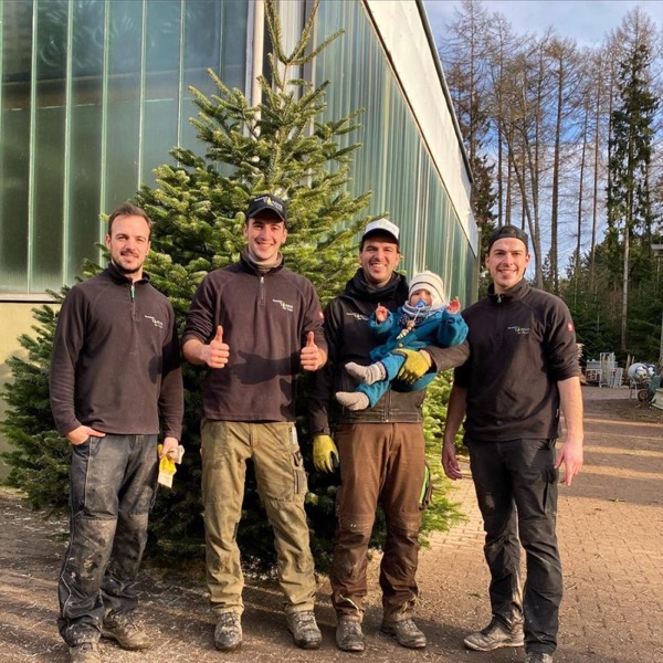 Das Team der Hunsrücktanne mit Baby vor einer großen Nordmanntanne